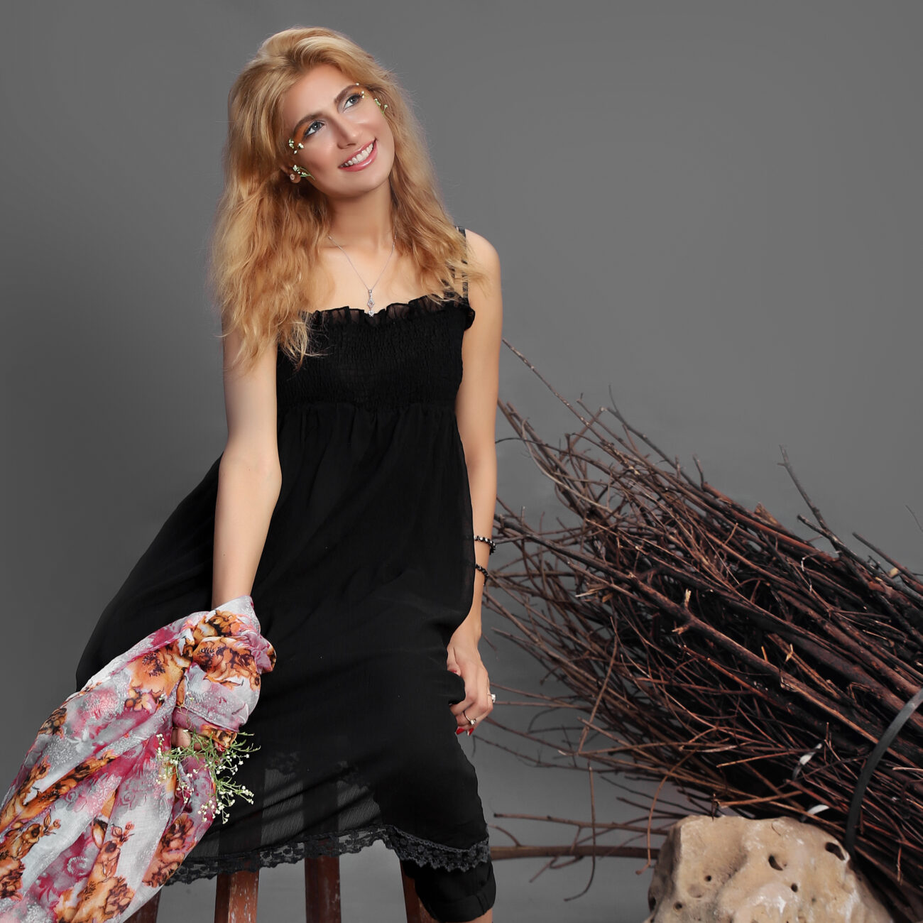 Fashion model with blonde hair wearing a sleek black dress and holding a designer handbag during a studio shoot.